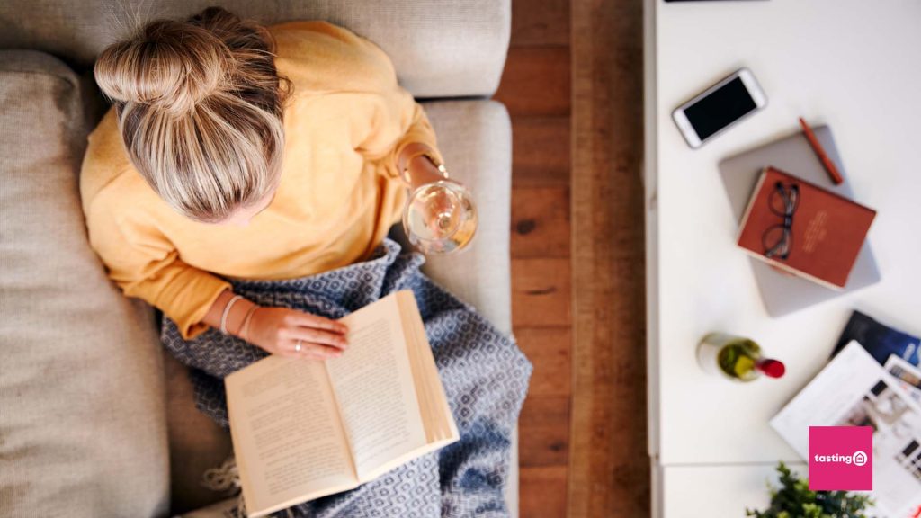 picture of a woman drinking wine and reading a book on the sofa
